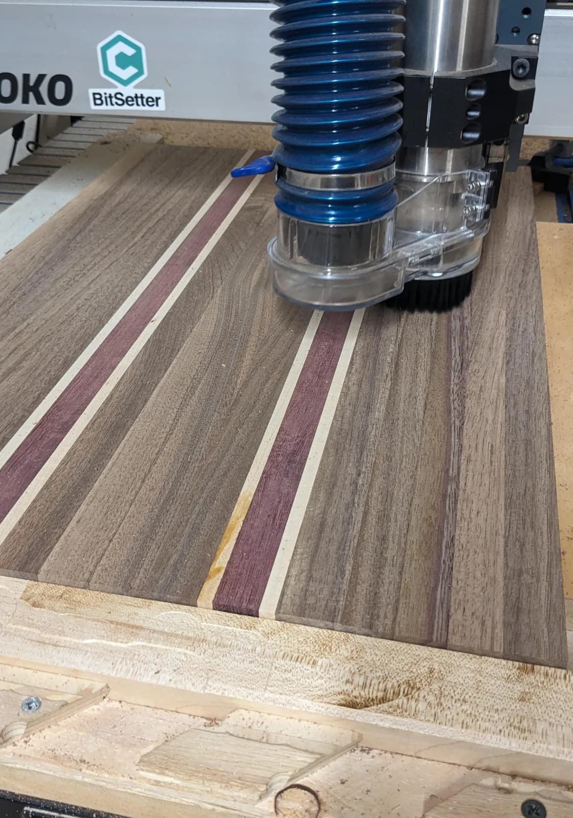 CNC machine work on bread serving board made from walnut, maple and purple heart wood species glued together.